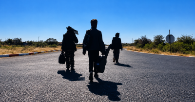 Musicians walking with instrument cases along a Maun road